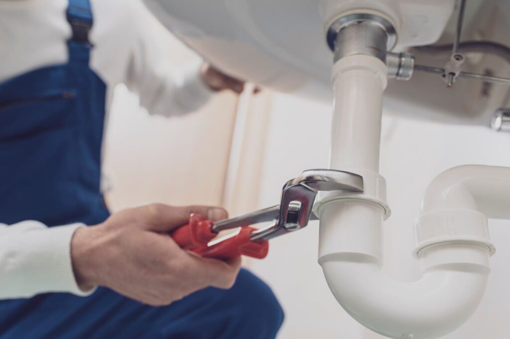 Plumber repairing a white drain pipe beneath a sink in Louisville